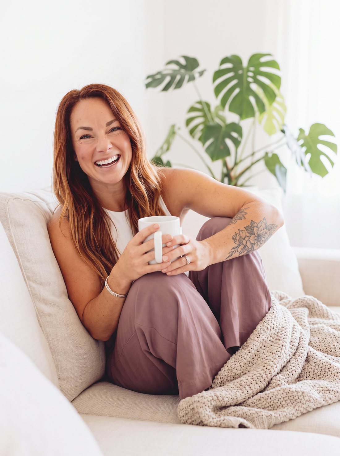 Ashley laughing on the couch with a mug and a blanket